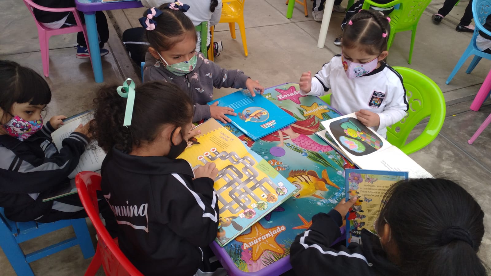 Cuatro niñas de colegio público del Distrito de Jesús María sentadas alrededor de mesa pequeña leyendo libros ofrecidos por la Biblioteca Viajera